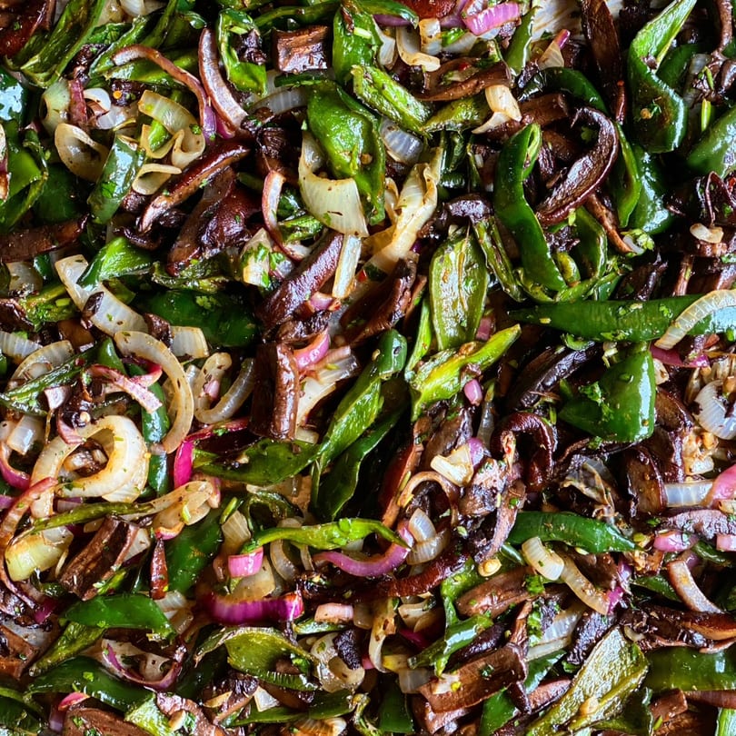 Close-up of sautéed green peppers, red onions, and white onions, with dark brown strips of meat.