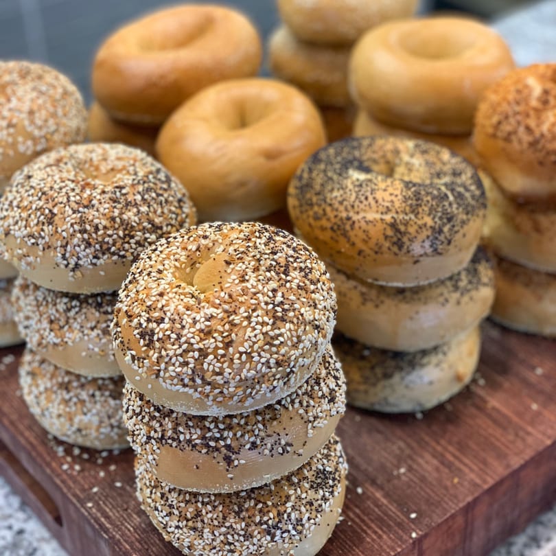 Stacks of fresh bagels, some plain, some topped with sesame seeds and poppy seeds.