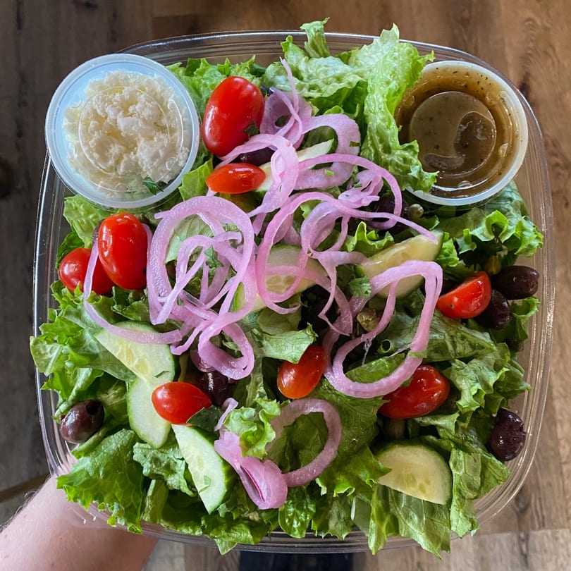 A Hungry Rooster Kitchen and Catering salad with lettuce, tomatoes, cucumbers, olives, pickled onions, feta, and dressing.