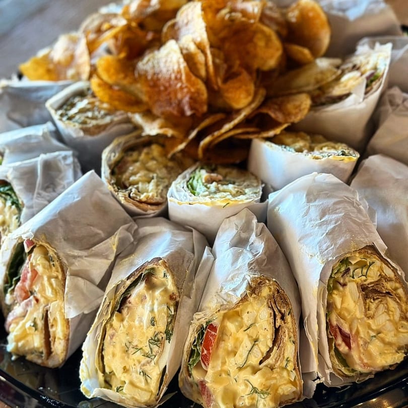 A catering platter of Hungry Rooster Kitchen wraps, cut in half, with a pile of potato chips.